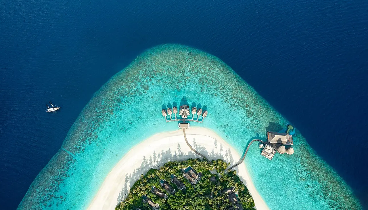 An aerial view of Anantara Kihavah Maldives Villas reveals a vibrant turquoise lagoon encircling the island, framed by soft white sands and